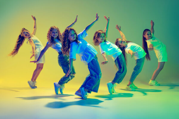 Group of active kids, cheerful girls dancing isolated over green background in neon light. Team dancing